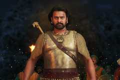 Baahubali in armor walks in front of a fire